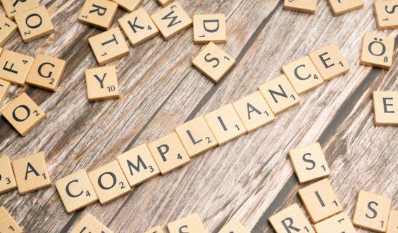 The word compliance spelled out with wooden letter tiles on a rustic table